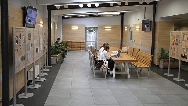 Zdjęcie korytarza w budynku wydziału z stolikiem i ławkami w tle