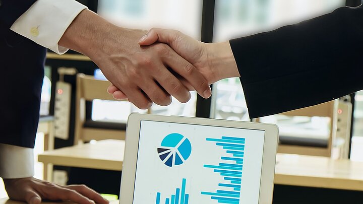 Zdjęcie dwóch rąk w uścisku na tle otwartego laptopa