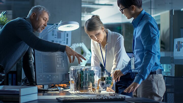 Zdjęcie grupy osób stojących przed stołem na którym leży skrzynka z mechanizmem w środku