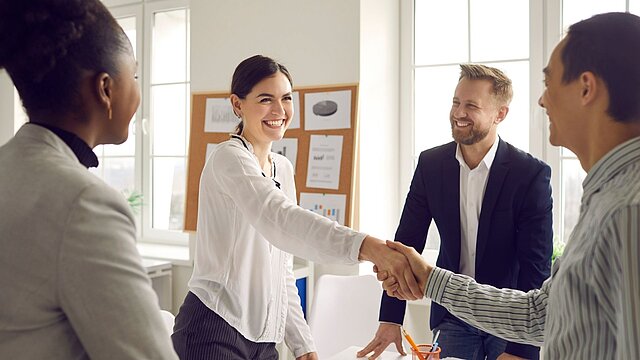 Zdjęcie czterech stojących osób z których dwie ściskają sobie dłonie