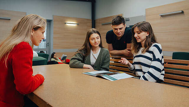 Grupa uśmiechniętych studentów pochylonych nad projektem
