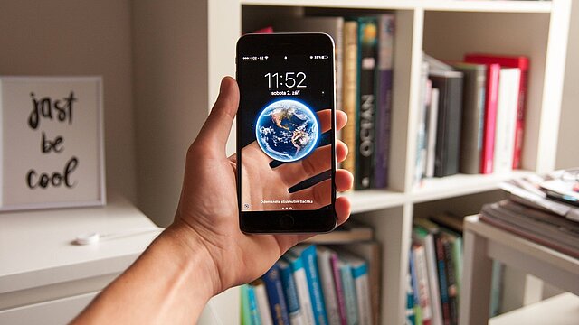 Zdjęcie dłoni trzymającej telefon komórkowy z kulą ziemską na wyświetlaczu