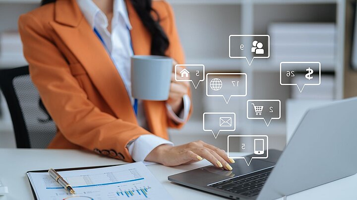 Zdjęcie kobiety trzymającej kubek i piszącej na klawiaturze z cyfrowymi ikonami wychodzącymi z klawiatury