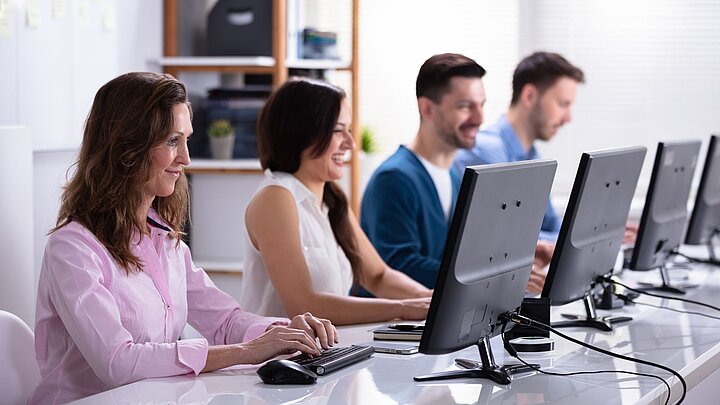 Zdjęcie grupy osób siedzących w lini przy stole z monitorami komputerowymi