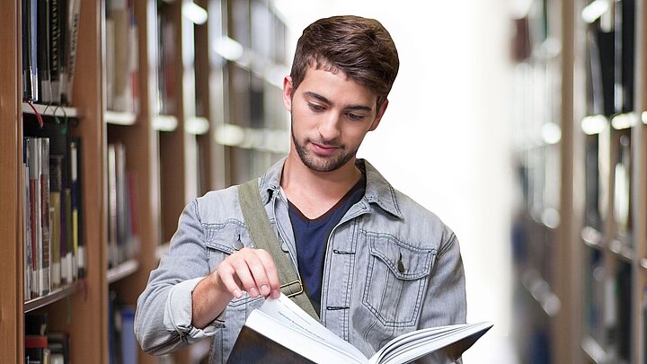 Zdjęcie studenta czytającego między półkami bibliotecznymi