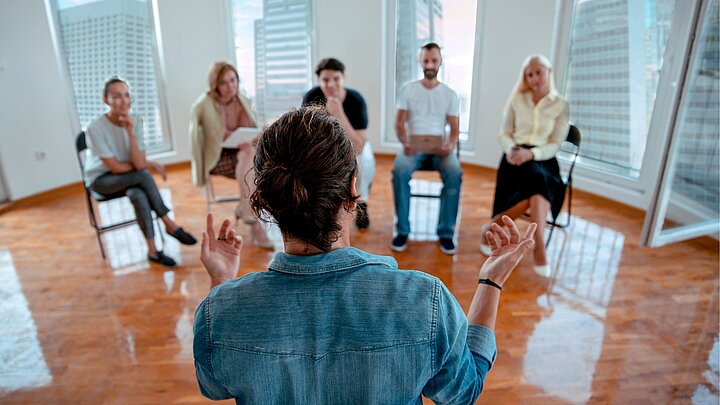 Zdjęcie zajęć warsztatowych na którym trener mówi do siedzących osób