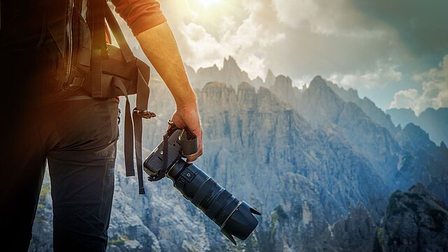 Zdjęcie fotografa trzymającego aparat na tle gór