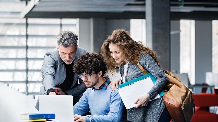 Zdjęcie drupy osób pracujących przy stole i spoglądających na monitor