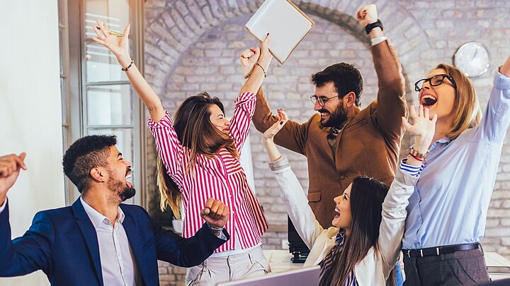 Zdjęcie grupy osób wiwatujących sukces z rękami uniesionymi do góry w geście triumfu