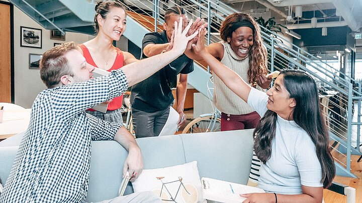 zdjęcie grupy studentów siedząścych na ławce i trzymających się za ręce w górnym uścisku