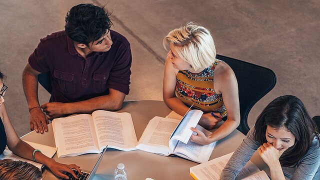 Zdjęcie trzech osób suiedzących przy stole na którym ułożone są książki