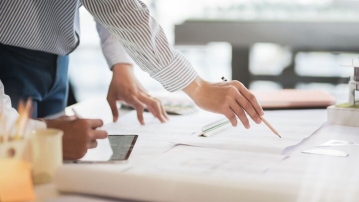 Zdjęcie osoby trzymającej ołówek w dłoni i piszącym po kartce leżącej na stole