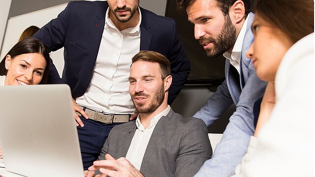 Zdjęcie grupy osób skupionych przy stone i patrzących z ekran laptopa