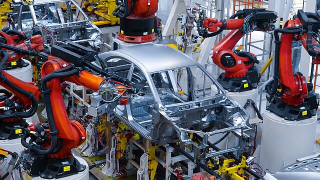 Zdjęcie karoserii samochodu otoczonej kilkoma robotami przemysłowymi