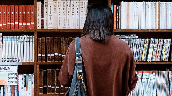Zdjęcie studentki czytającej przed półkami bibliotecznymi