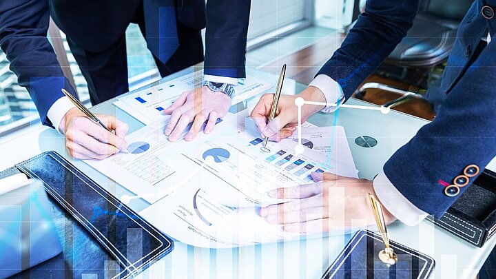 Zdjęcie grupy osób pochylonych nad stołem i rysujacych wykresy