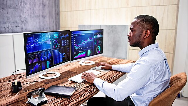 Zdjęcie osdoby siedzącej przed dwoma ekranami komputerowymi