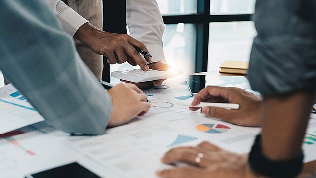 Zdjęcie trzech osób pochylonych na blatem na którym leżą dokumenty