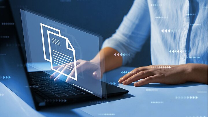 Zbstrakcyjne zdjęcie osoby siedzącej przed laptopen nad którym unoszą się ikony dokumentów