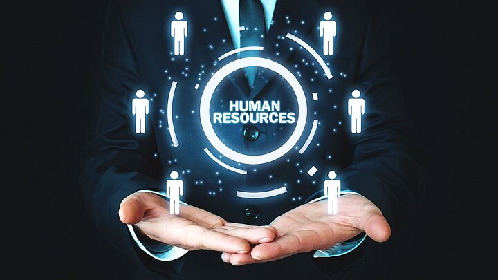 Zdhęcie dłoni podtrzymujących wygenerowany cyfrowo napis hjuman resourses otoczony kołem z ikonami