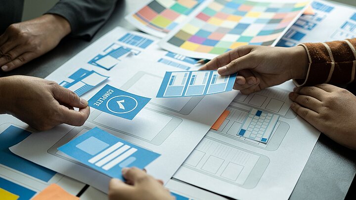 Zdjęcie stołu na którym leżą dokumenty nad którymi dwie osoby przekazują sobie karteczki