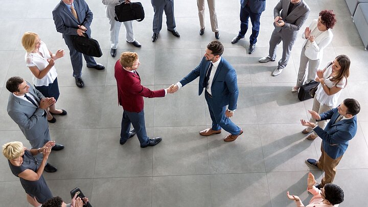 Zdjęcie grupy osób ustawionych w okręgu oraz dwoma osobami w środku podającymi sobie ręce