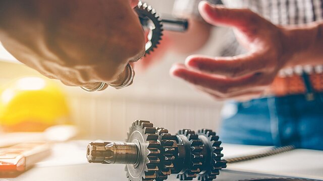 Abstrakcyjne zdjęcie mechanizmu zębatego i dłoni przekazujących go sobie