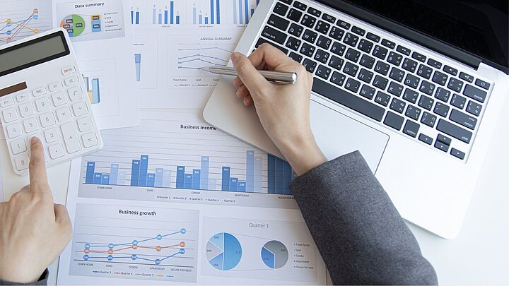 Zdjęcie z góry przedstawiające stół na którym leżą kartki z wykresami i laptop